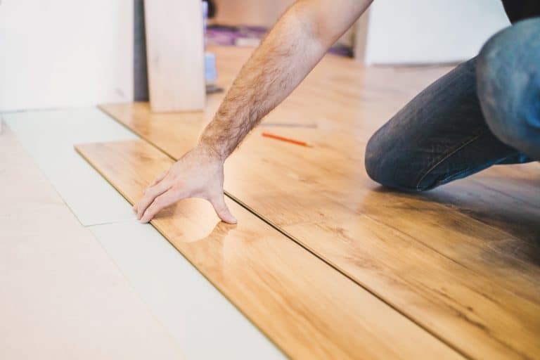 A man installing vinyl flooring plank on the floor over old-battered tiles, Is Vinyl Plank Flooring Durable Enough for Dogs?