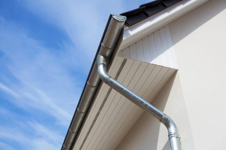 A galvanized iron gutter with a metal downspout on a gable roof design, How Much Does It Cost To Realign Gutters?