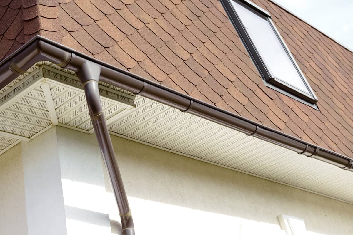 A house with asphalt shingles and a small steel gutter with a galvanized iron down spout, Are My Gutters Too Small? (Inc. How To Increase Gutter Capacity)