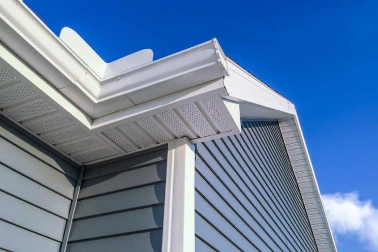 A low angle view of soffit, gutters, downspout and vinyl siding on a new home. Blue sky is in the background, Can Faded Vinyl Siding Be Painted? [3 Things to Consider]