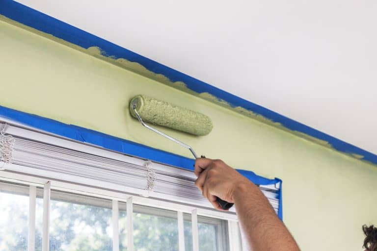 A painter painting with a light green color to the wall and taped the ceiling corners to avoid smudging paint on it, How to Not Get Paint on Ceiling When Painting the Walls [4 Tips]