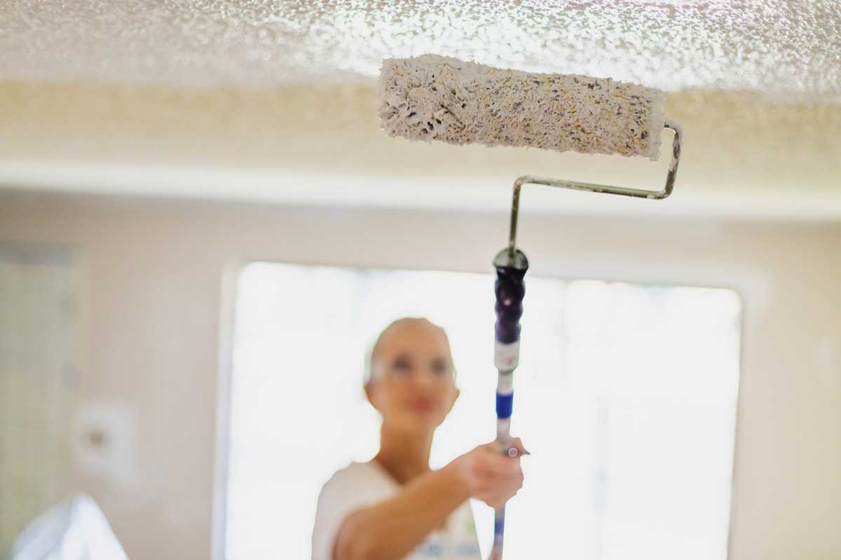 Mature Adult Female Painting Popcorn Ceiling White With Paint Roller;How to Cover Popcorn Ceiling? [5 Steps]