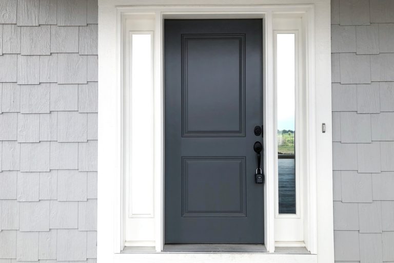 A dark gray colored door with a white painted door frame and decorative wooden vinyl on the porch, How to Fill The Gap Between Door Trim And Wall?