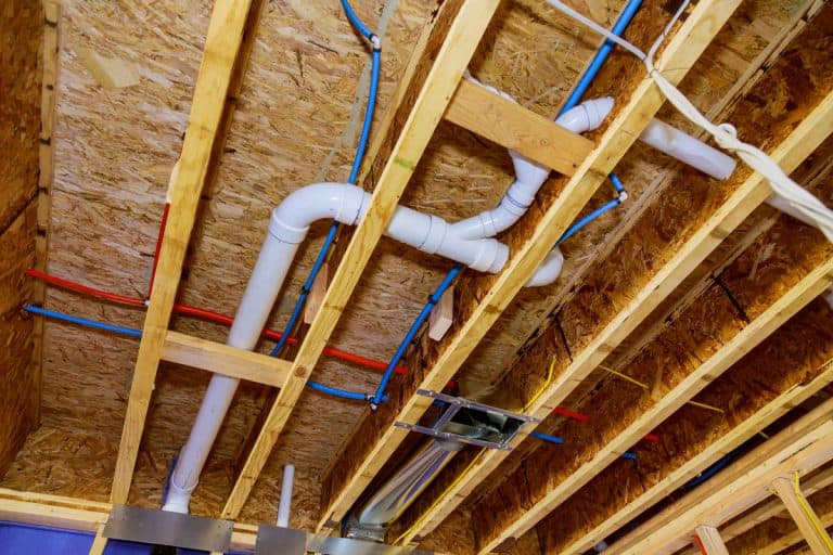 Series of PEX pipes running through the ceiling of a house next to plumbing lines, Can You Mix PEX And Copper Pipes?