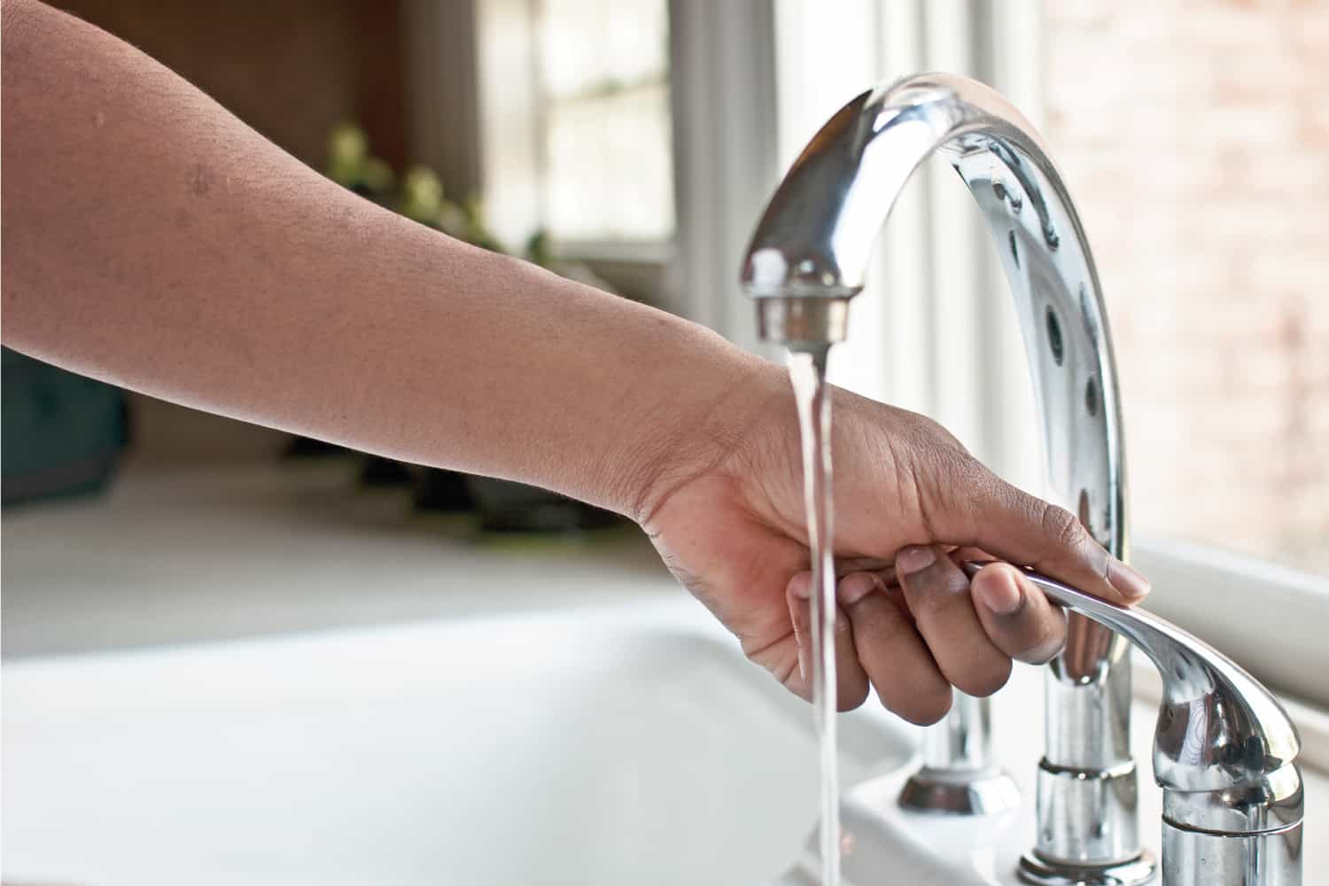 Close up of a left hand holding a push pull faucet near a window