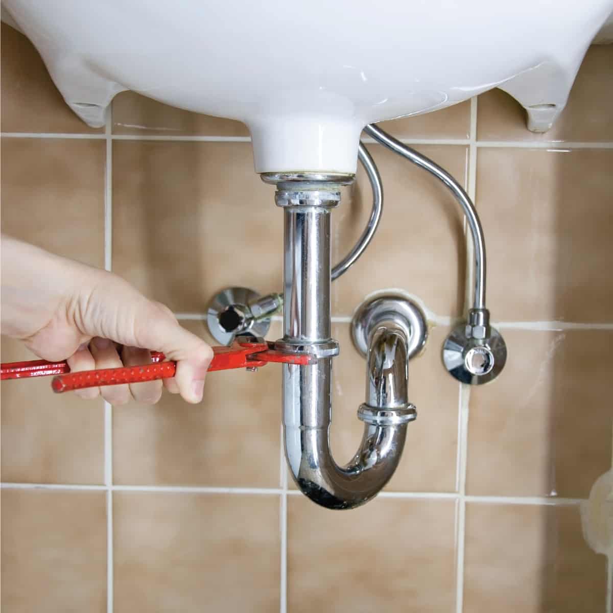 plumber with wrench loosening drain on a sink