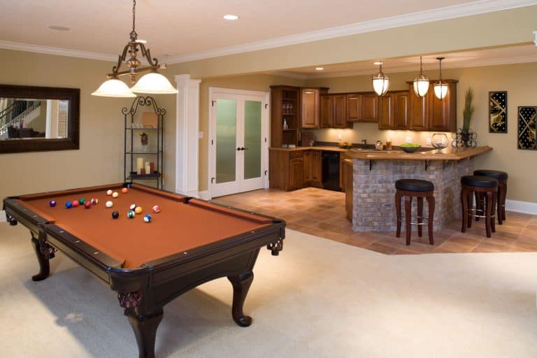 Interior of a basement with an entertainment area, a billiard table, and elegant dangling lights on the pantry area, Can You Finish A Basement With Low Ceilings?