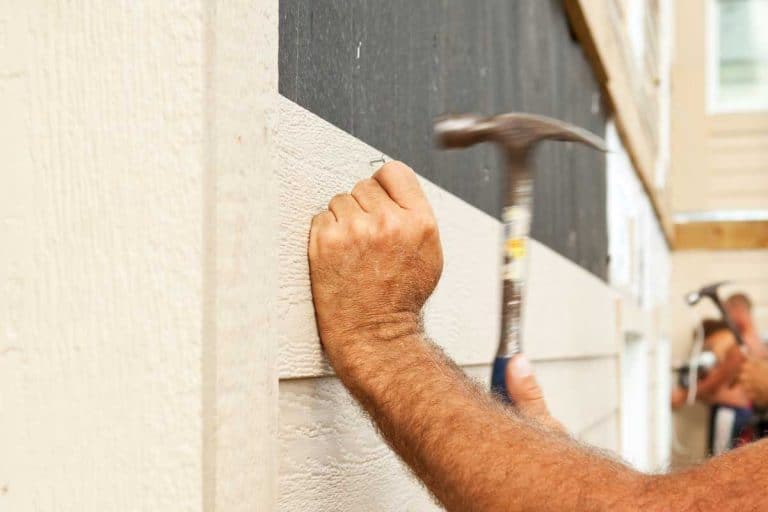 A construction worker using hammer installing siding onto a tar paper covered exterior house wall, What Nails Should I Use For Wood Siding?