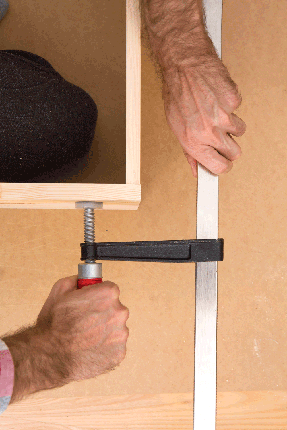 woodworker using bar clamp on his cabinet project