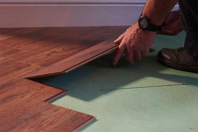 A workman laying a piece of new laminate flooring, Can You Glue Down A Floating Floor?