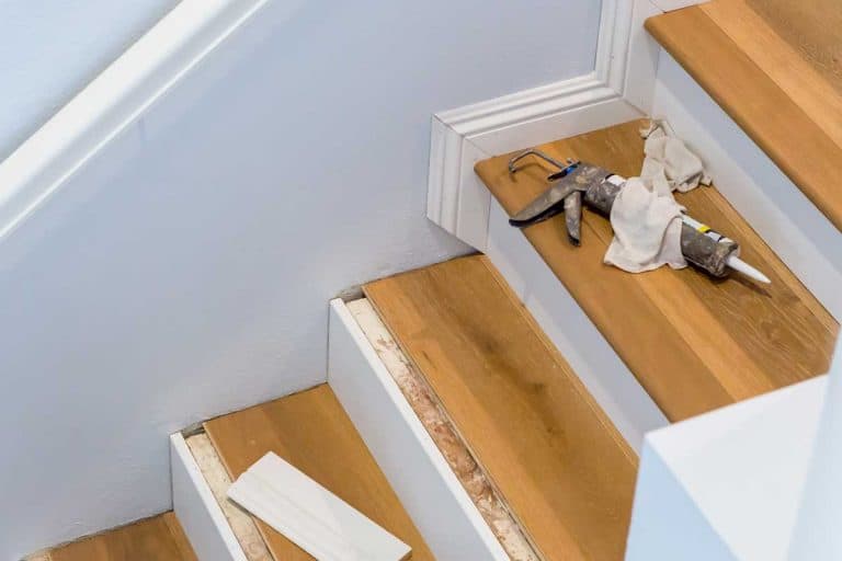 Hardwood floor installation on stairs with caulking gun on step