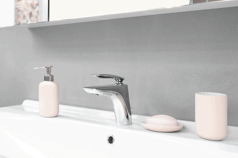 Luxury modern style faucet mixer on a white sink in a beautiful gray and white bathroom with pink glass accessories. How To Get Rid Of Ants In A Bathroom Sink