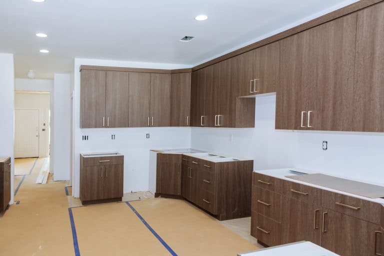 Oak wooden cabinetry inside a white walled kitchen area with unfinished flooring, Should You Put Flooring Under Cabinets?