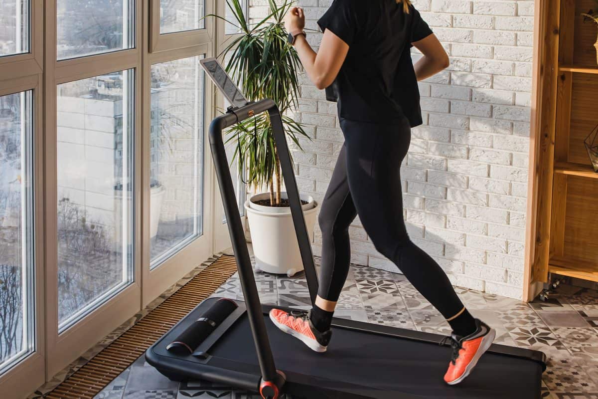 Young woman jogging on the modern compact treadmill at her home at room with big windows, Can You Have A Treadmill On The Second Floor?