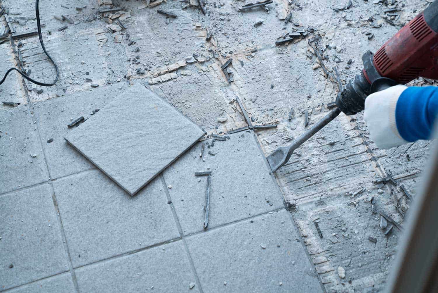 Construction worker using a handheld demolition hammer and wall breaker to chip away and remove old floor tiles during renovation work