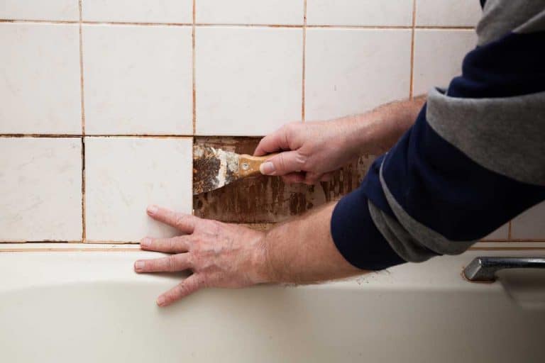 Man using a scraper to remove old bathroom shower tiles, How To Remove Tile And Grout From Floor