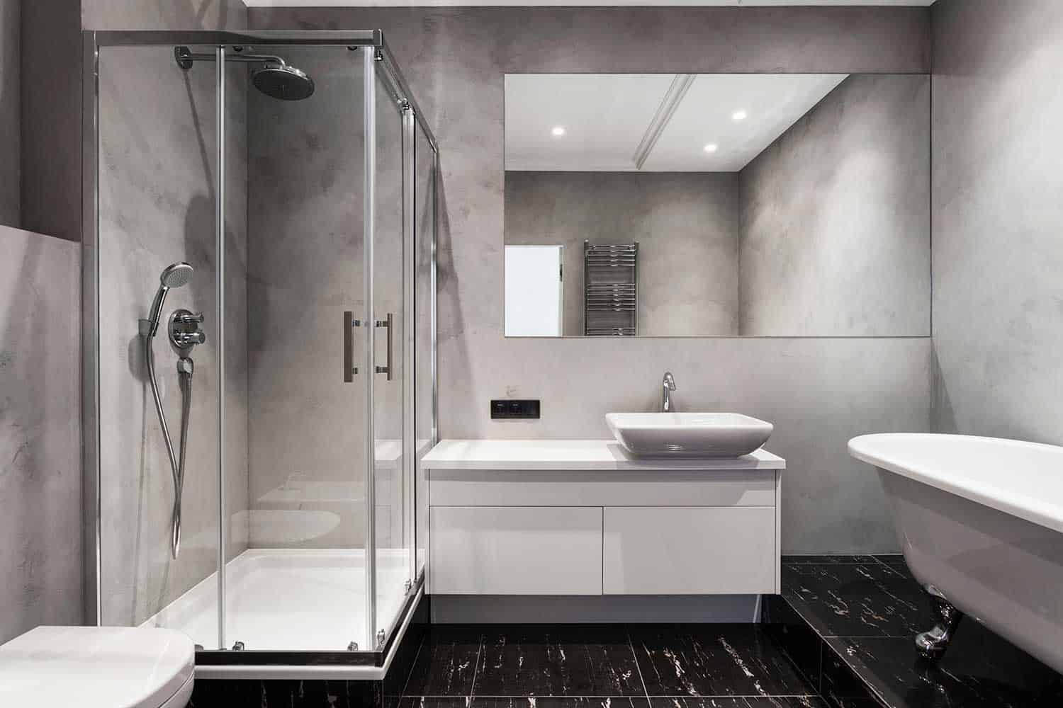 Bathroom with basin, shower cabin, large mirror and chrome silver heater at gray wall