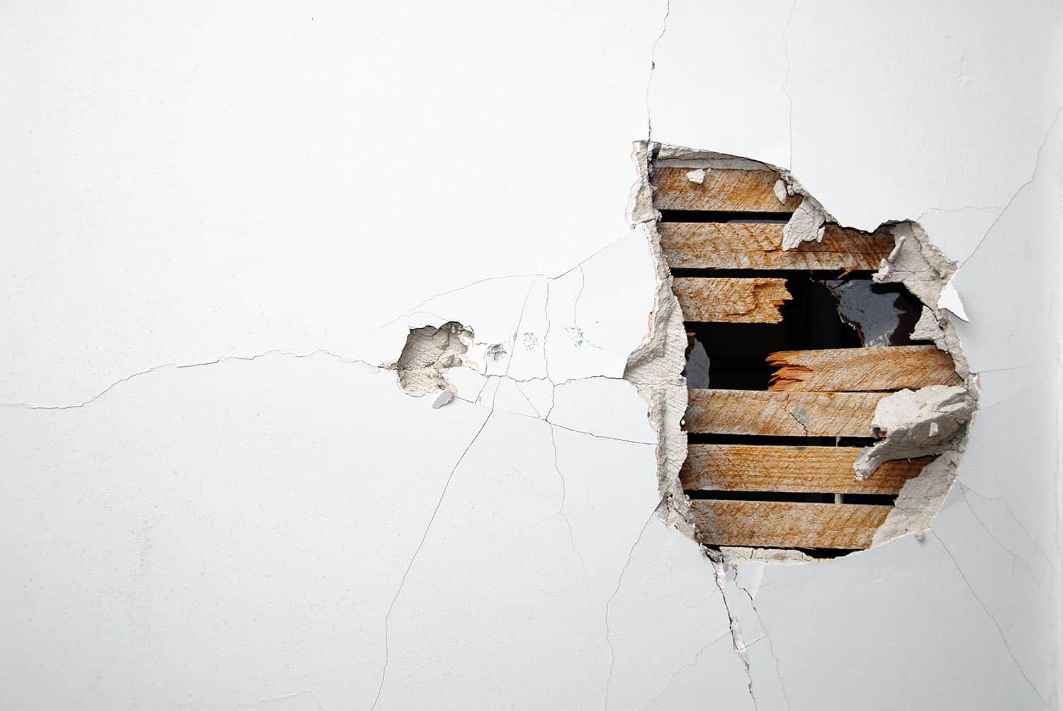Cracked plaster drywall and wood of a home's white wall