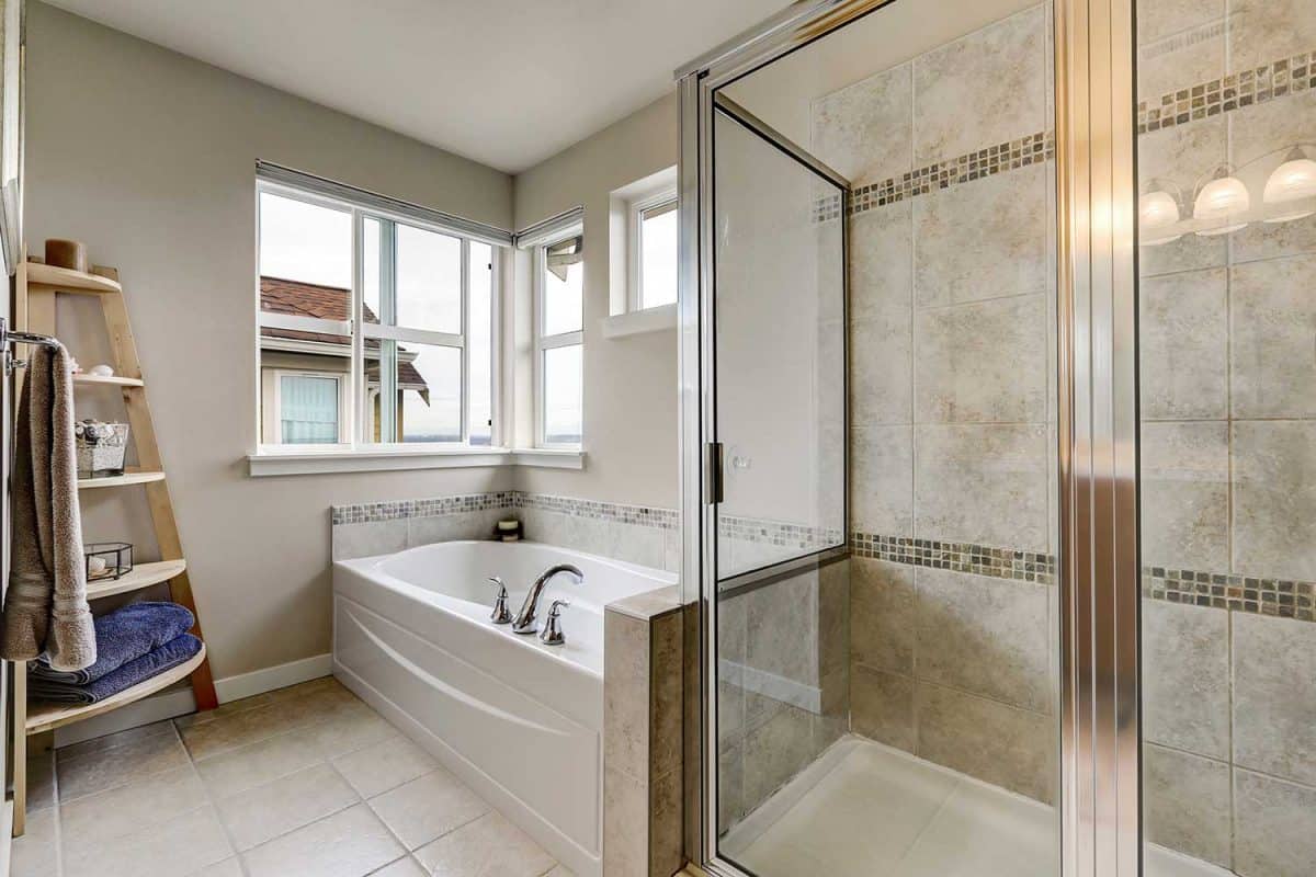 Glass shower and white bathtub in clean bathroom interior with mosaic tile trim