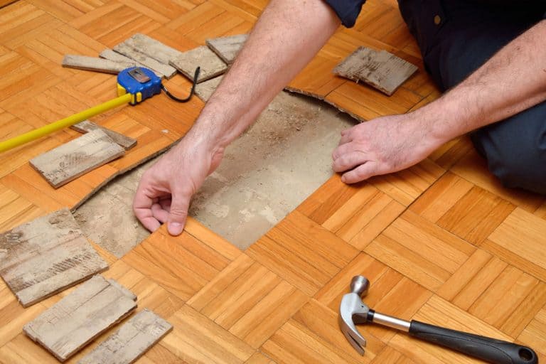 Man removing damaged pieces of wooden flooring, How To Remove Glued Down Wood Flooring