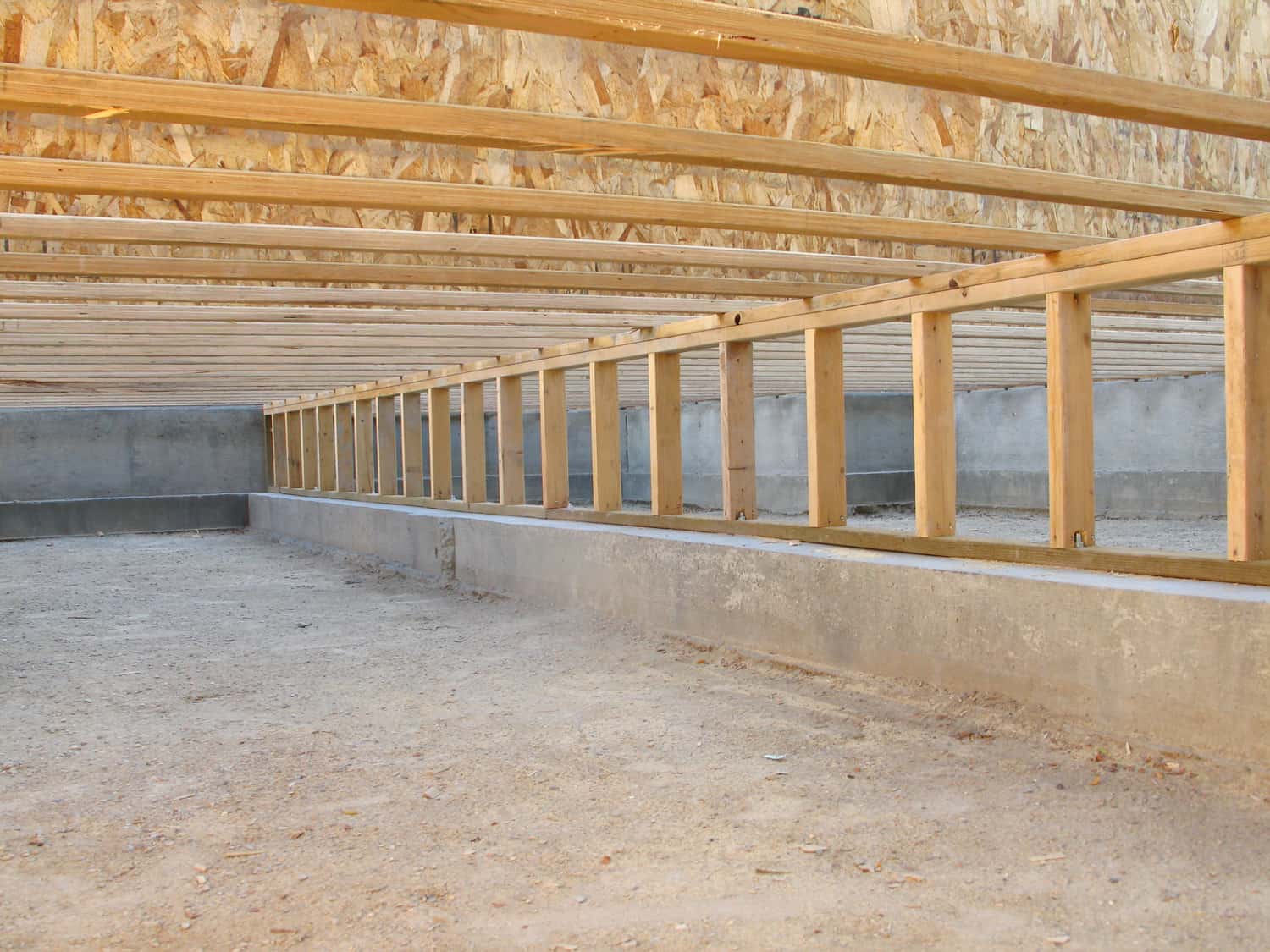 This color photo shows a view of the crawlspace foundation beneath the framing of a new house under construction. 