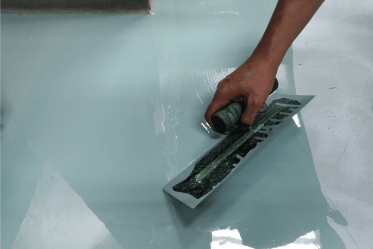 Construction worker painting the floor using self-leveling epoxy spreading with trowel. Best Epoxy Coating Products For Concrete Floors [7 Fantastic Choices]
