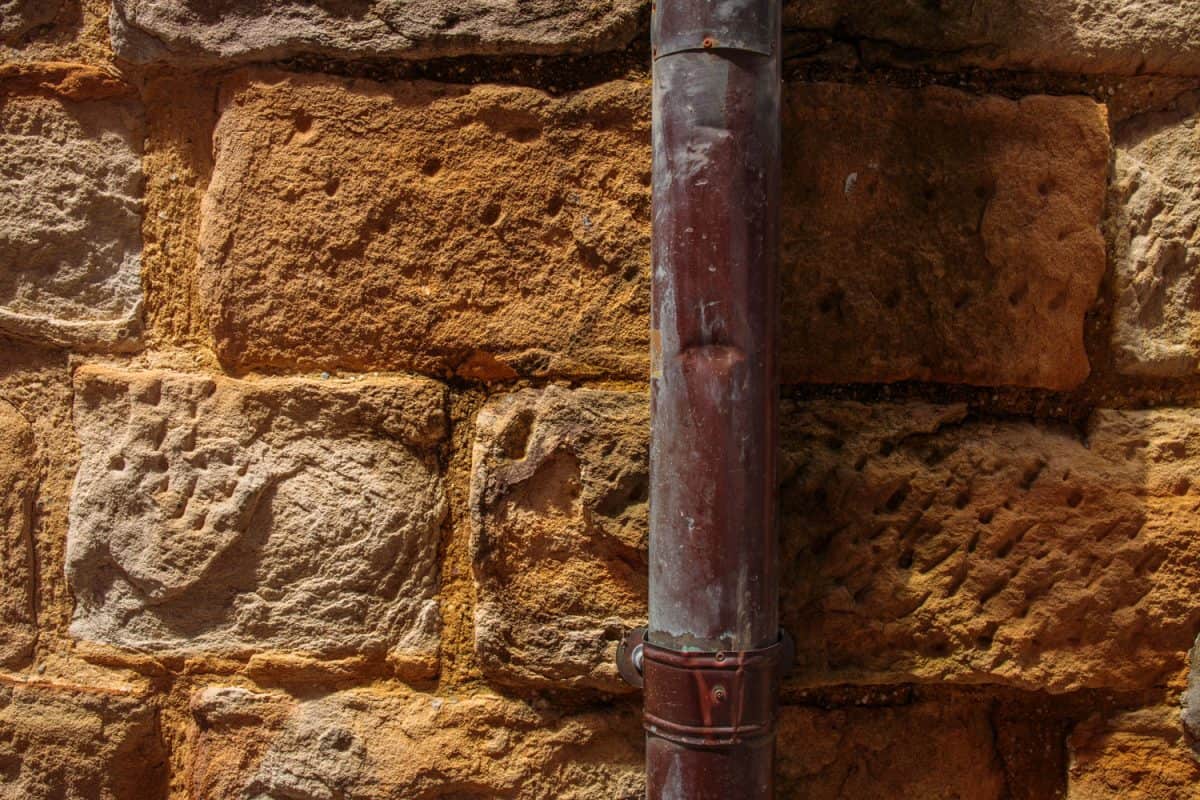 A rusted copper pipe installed in the brick wall