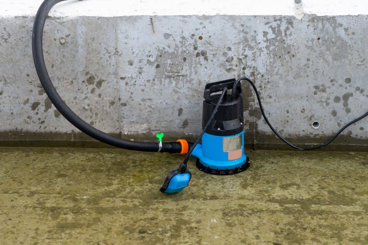 A sumbersible water pump set up outside a concrete next to a flooded portion of the construction site
