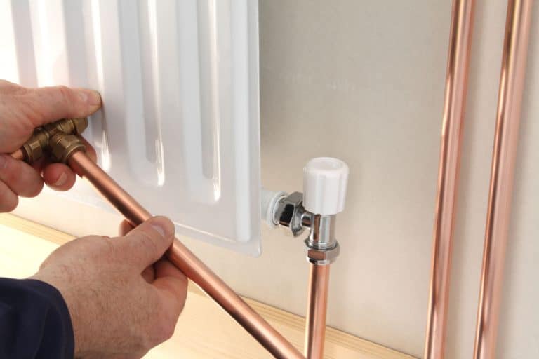 An electrician installing a copper pipe into the radiator of the central heater, How To Keep Copper Pipes Shiny? [Plus Natural Methods & Oxidation Prevention]