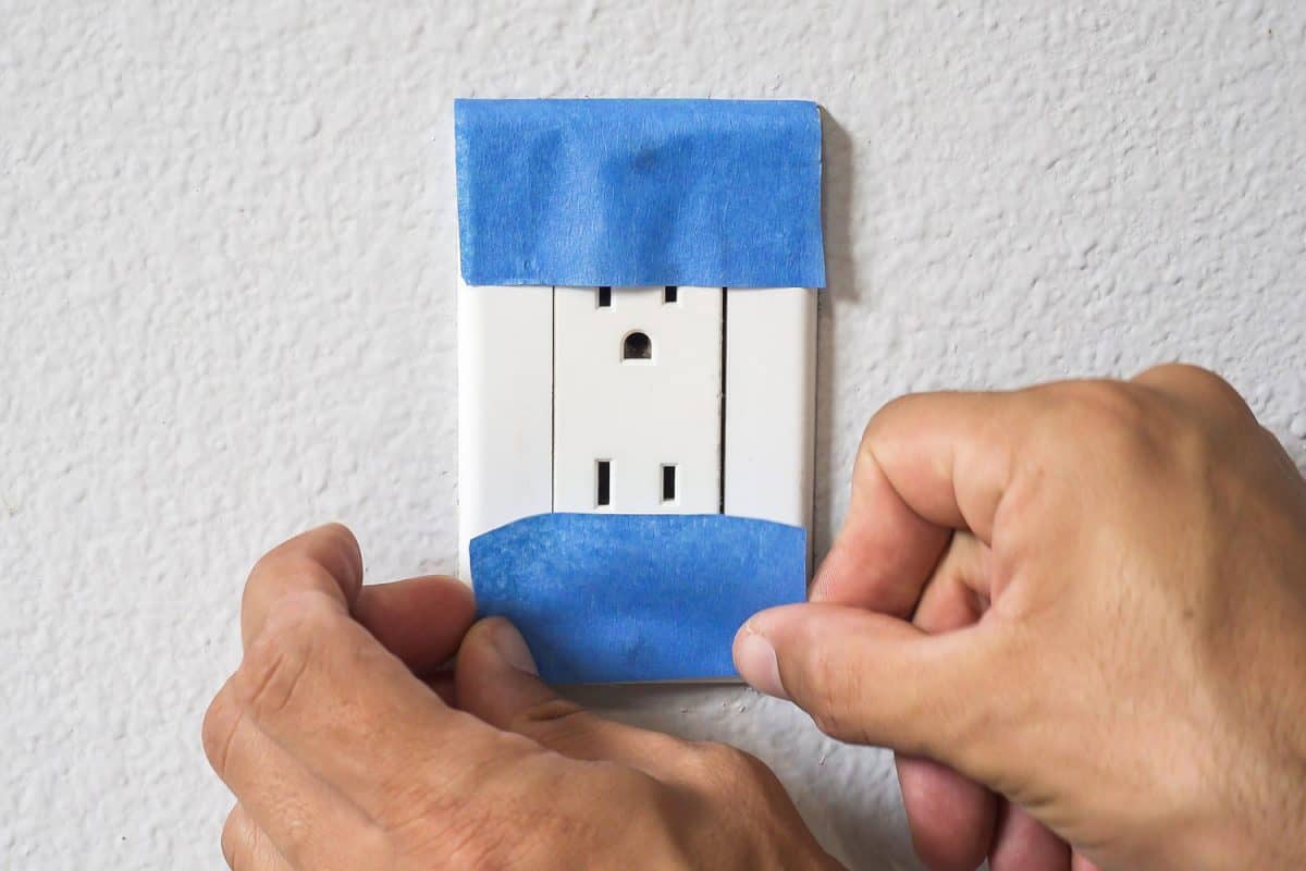 Painter Man Using Masking Blue Tape to Secure Power Outlet