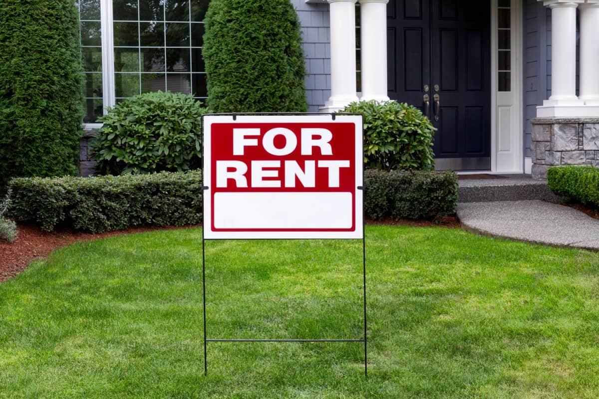A For Rent sign on the grass in the front yard of a house