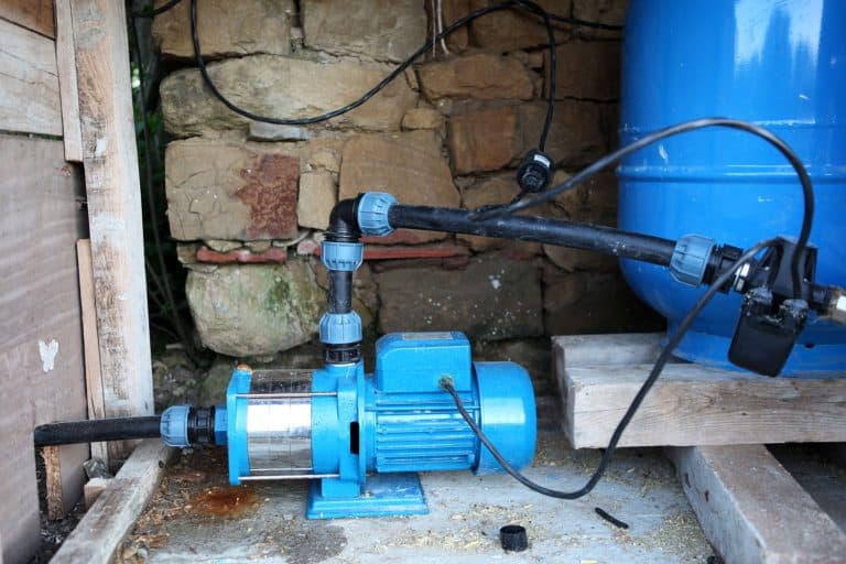 A blue well pump photographed in the back of the house, How Much Water is Needed to Prime a Well Pump?