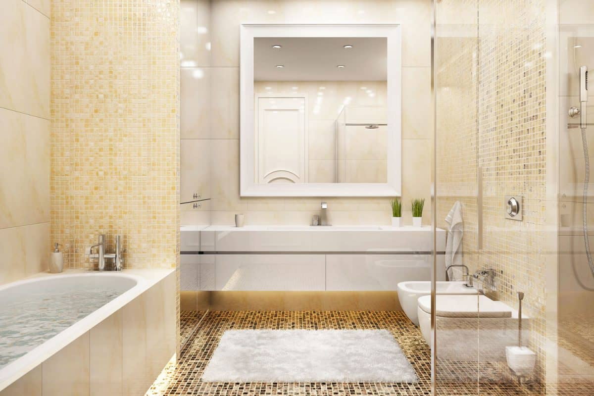 A bright and light yellow themed bathroom with a glass wall on the toilet area and a gorgeous backsplash on the bathtub