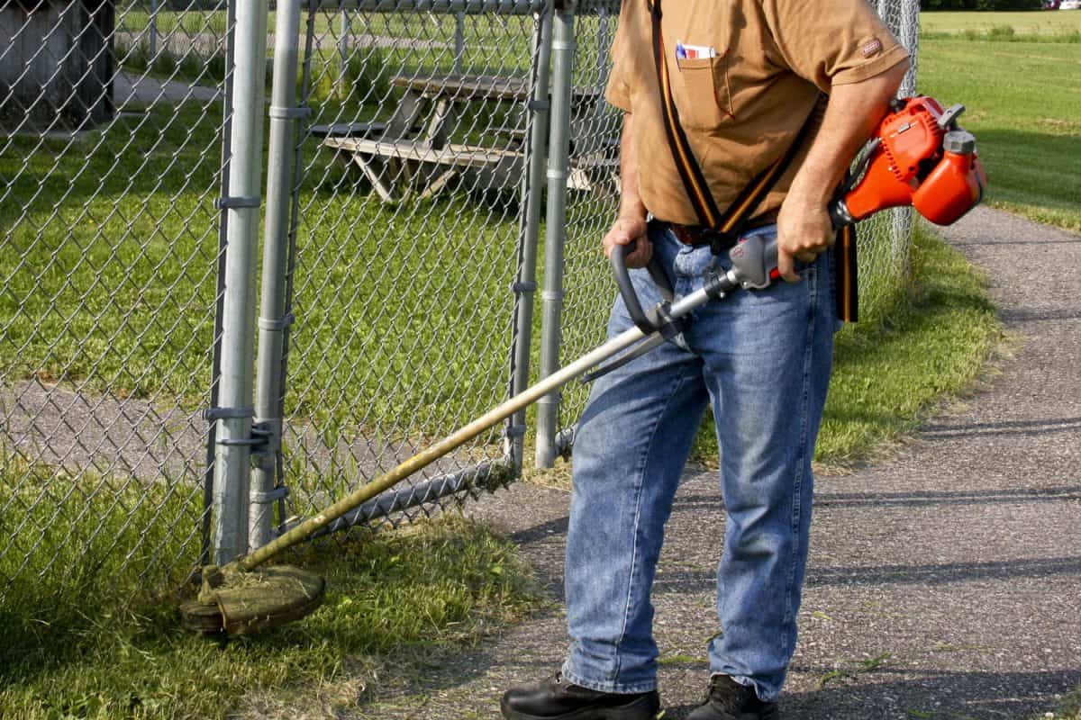 A grounds keeper trimming the grass around the fence