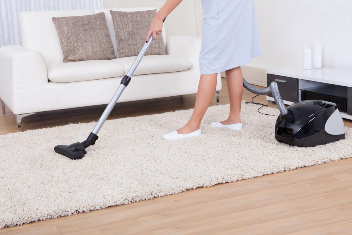A woman cleaning the white carpet using a vacuum