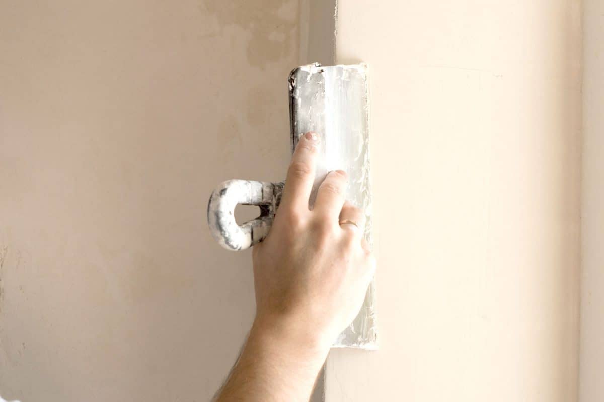 A worker applying sealant to the plastered wall