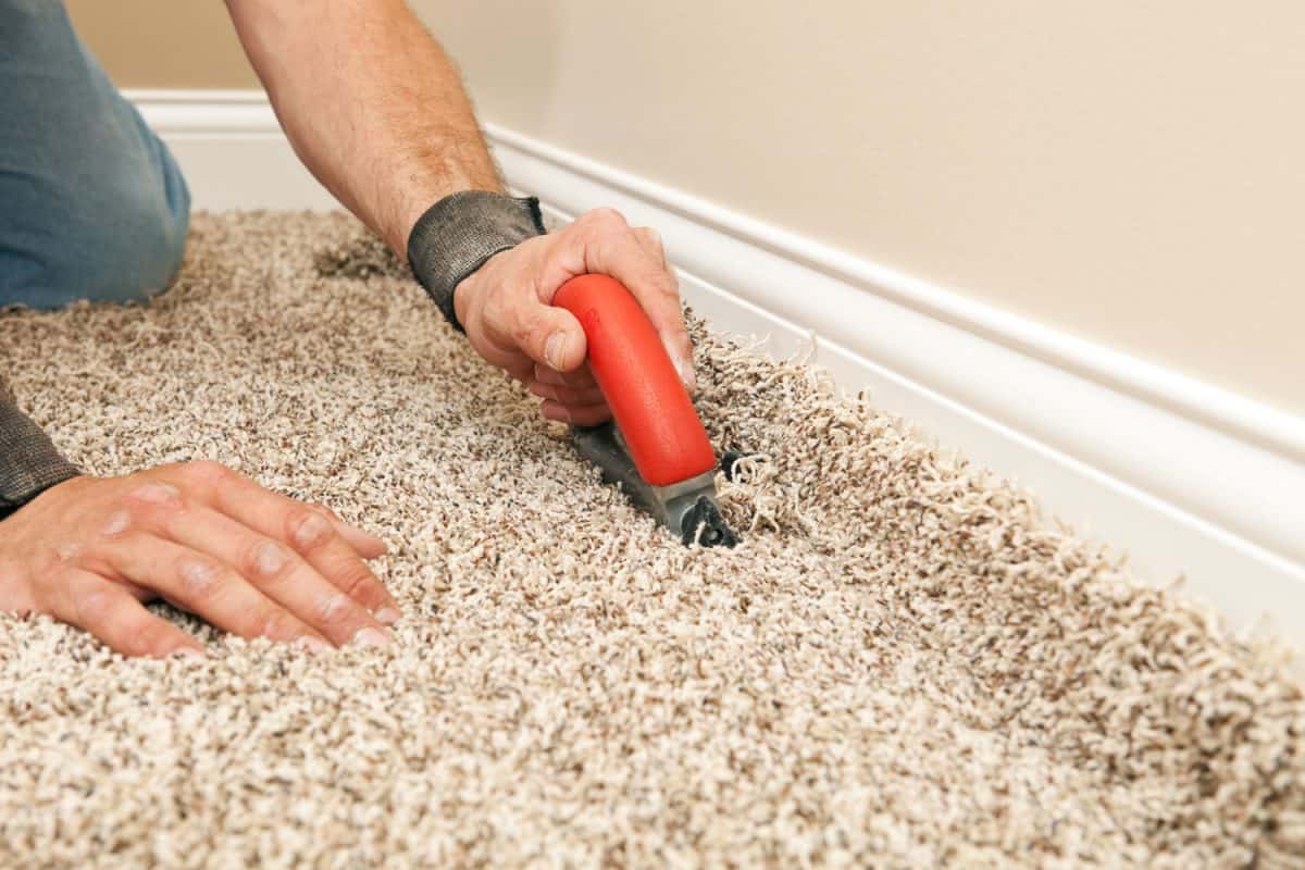 A worker cutting the excess carpet near the baseboard