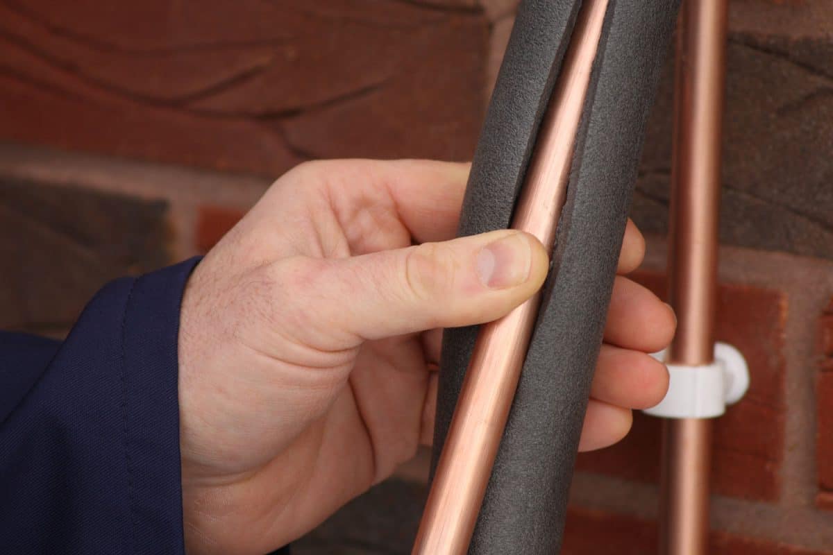A worker installing copper pipe insulation
