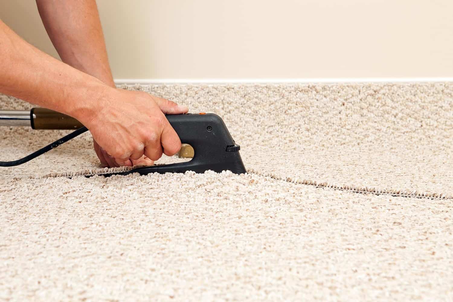 Carpet installer is using a seam iron to join two sections of berber carpet in a bedroom