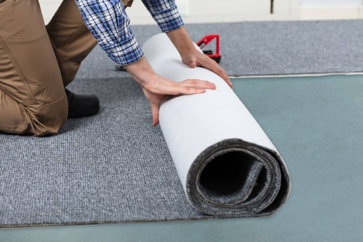 Carpet installer unrolling a gray carpet on the living room