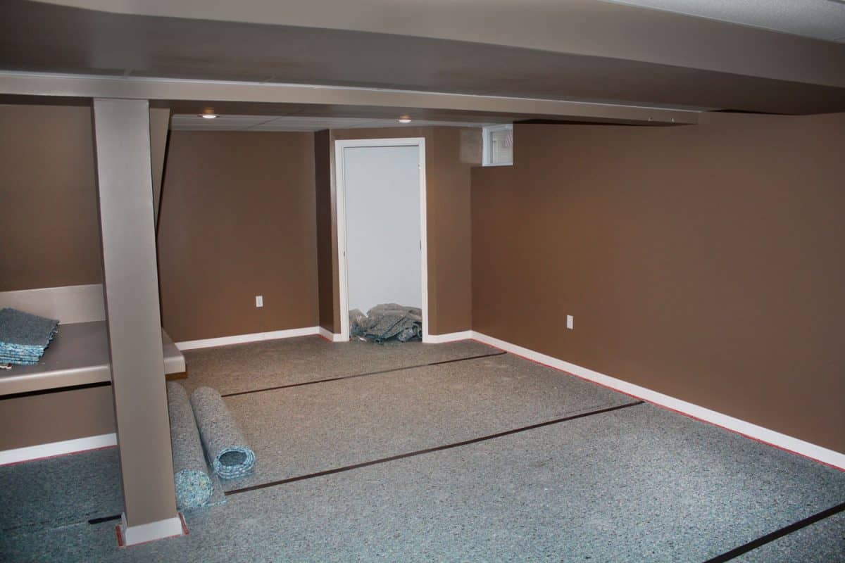 Interior of an empty living room with unfinished carpet padding, brown walls, and white trims