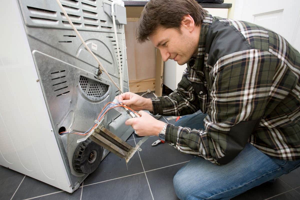 Repairman fixing a heating elelment on a domestic tumble dryer