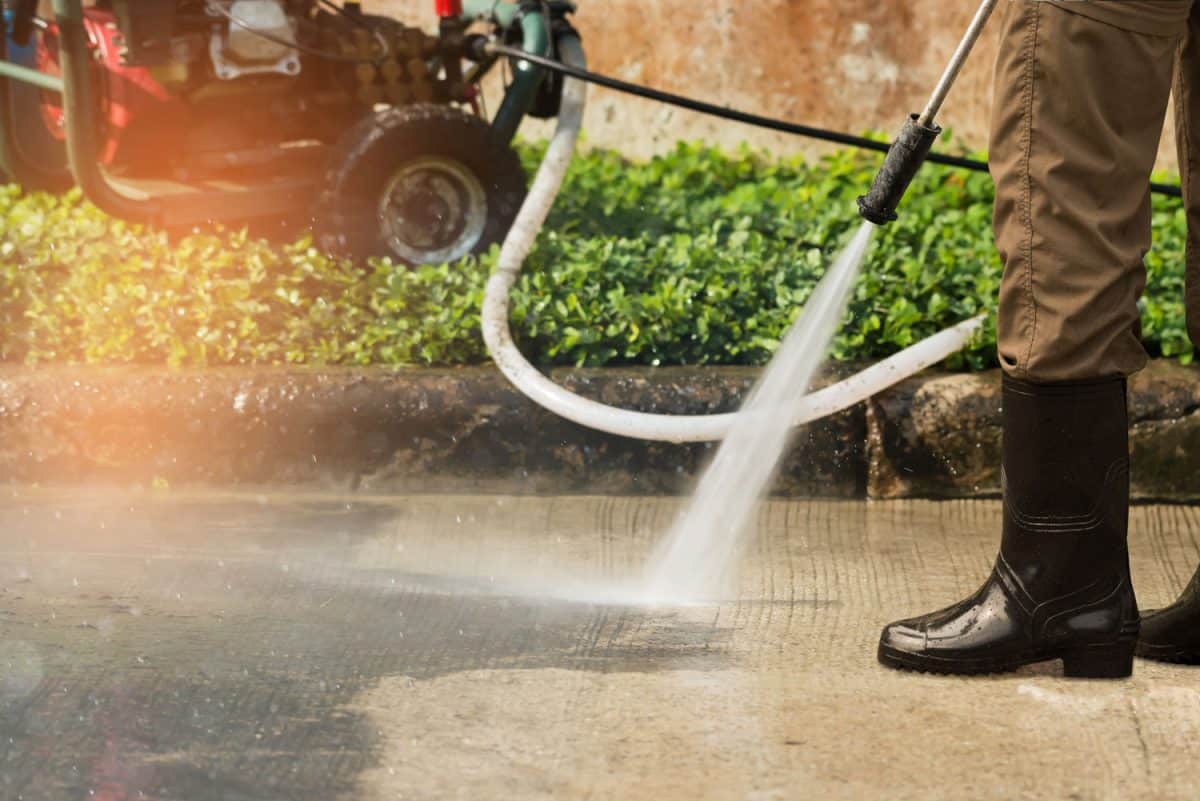 Worker cleaning driveway with gasoline high pressure washer splashing the dirt