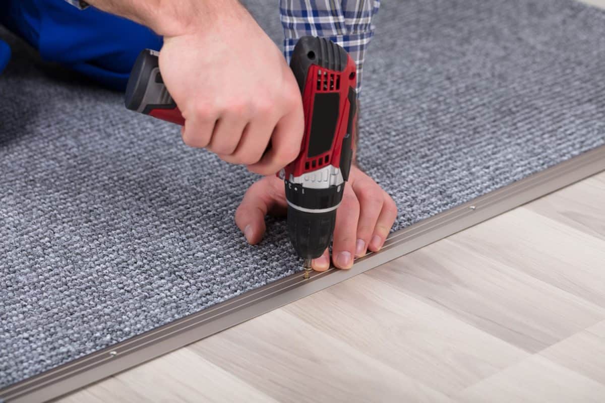 A carpet installer using a cordless power drill to install the carpet padding