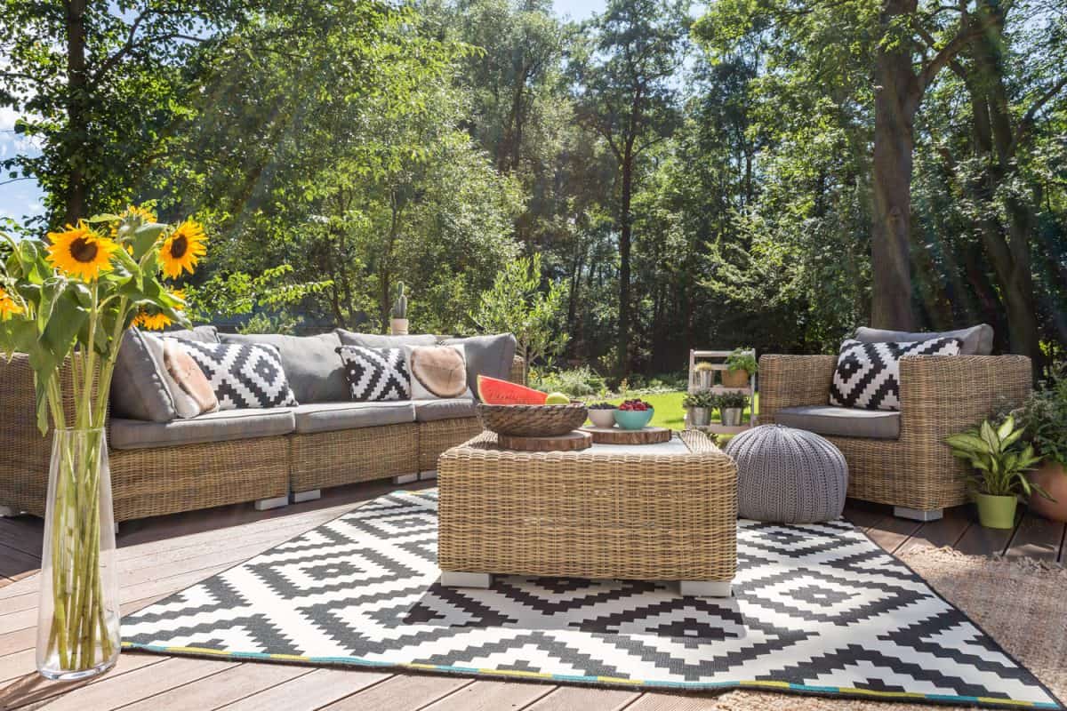 A gorgeous outdoor lanai with wicker chairs, throw pillows and black & white patterned carpet