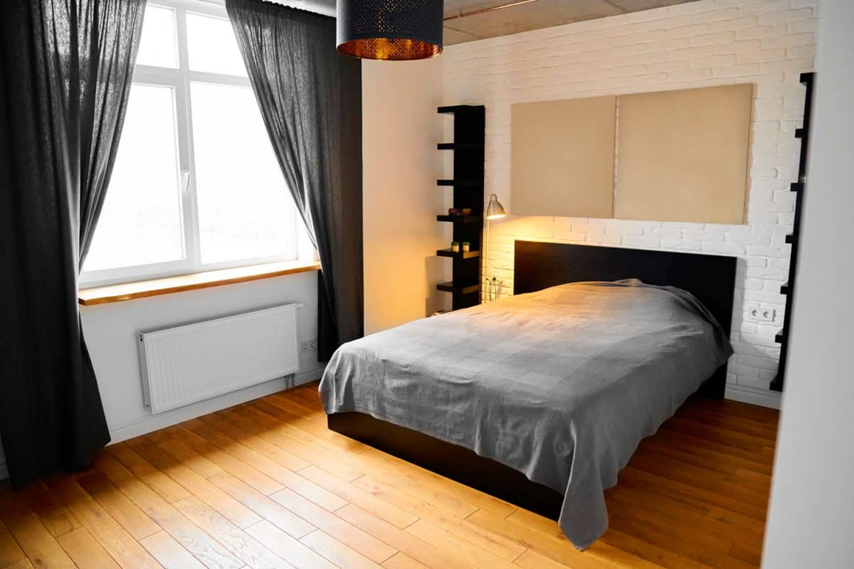 A small modern bedroom with wooden flooring gray beddings and curtains with white painted walls