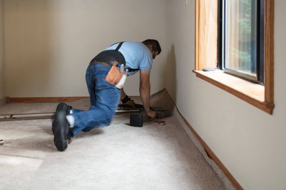 A worker installing the carpet using a knee kicker