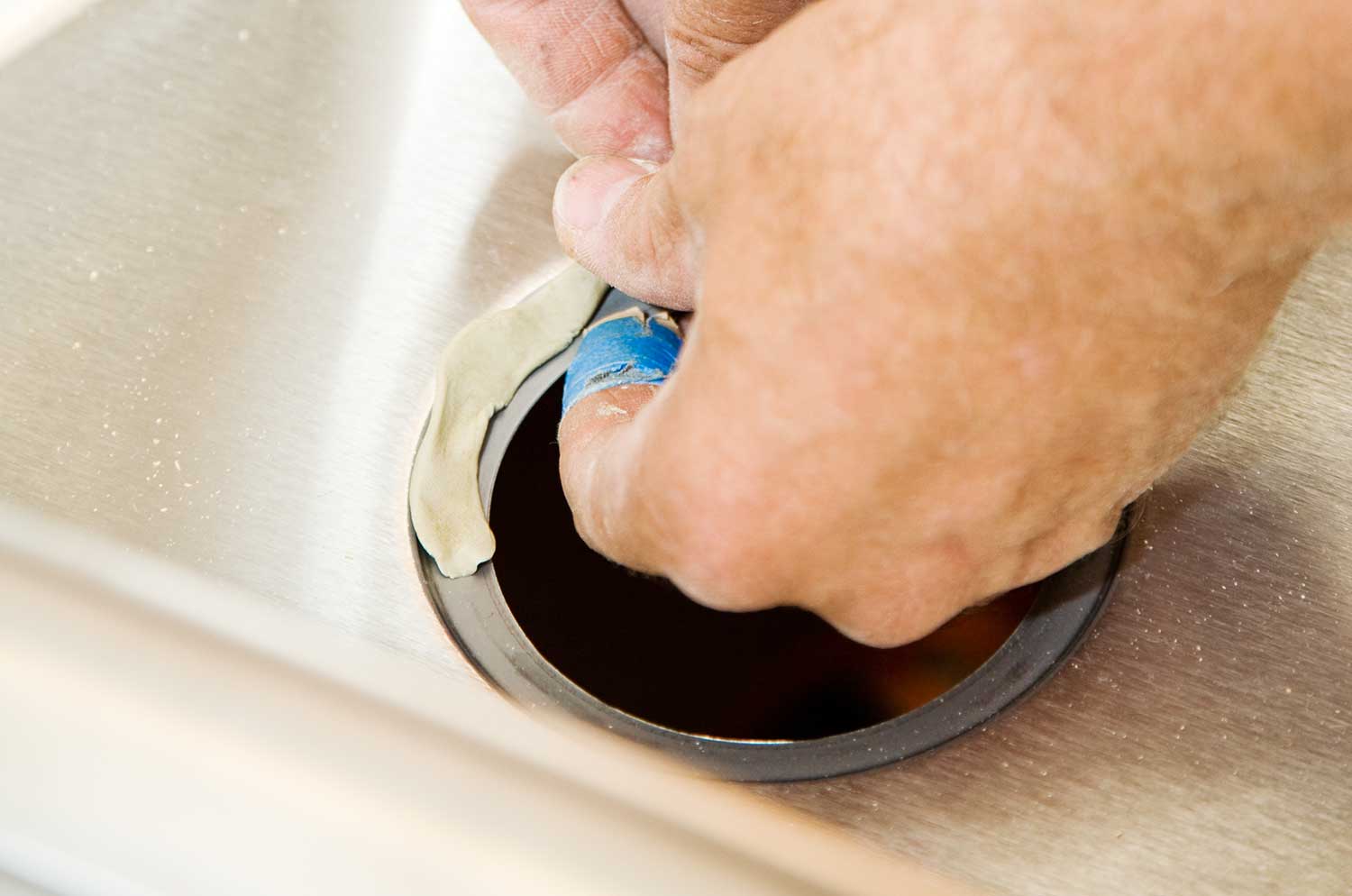 Closeup of a plumbers hands applying plumbing putty to sink drain