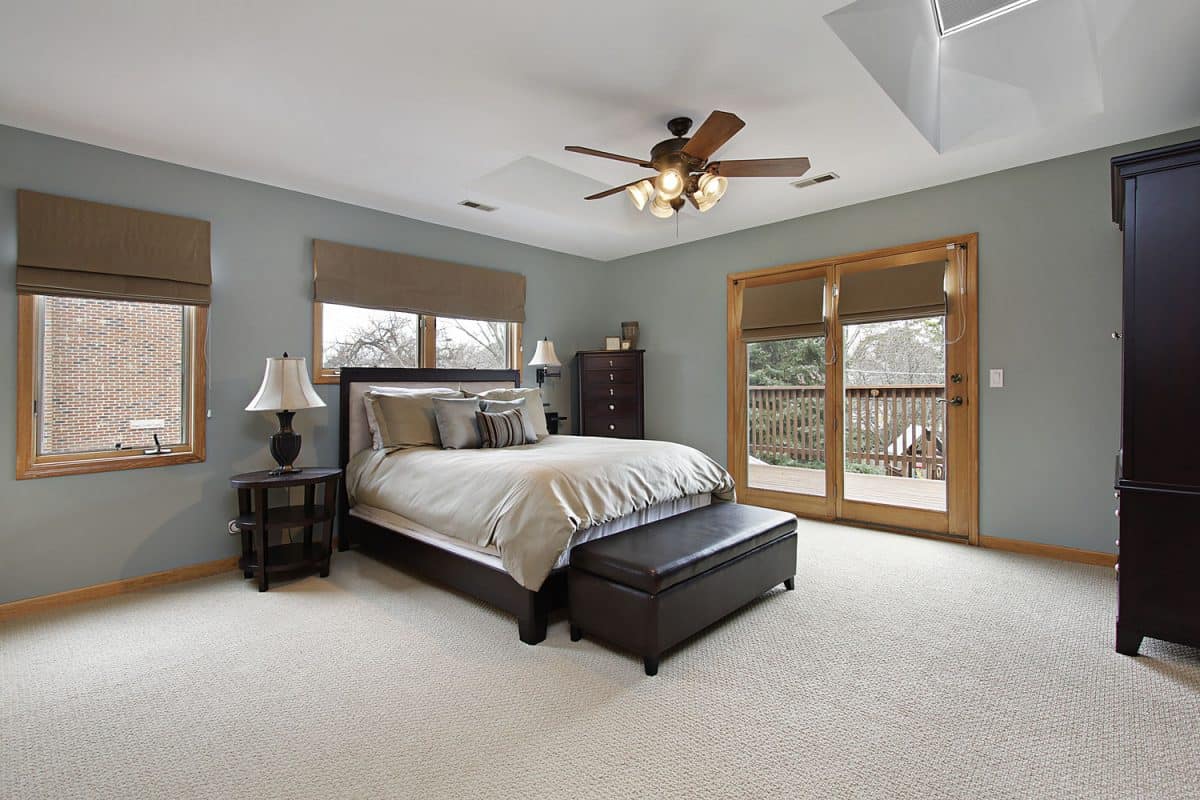 Cozy and rustic bedroom interior with carpeted flooring, gray walls with wooden framed windows and a ceiling fan