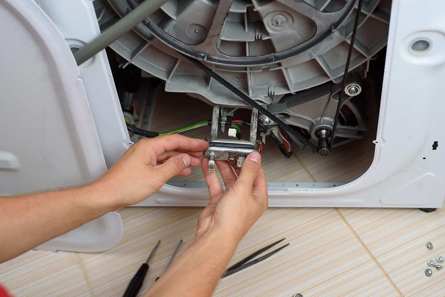Handyman repairs the washer machine with wrench and screwdriver